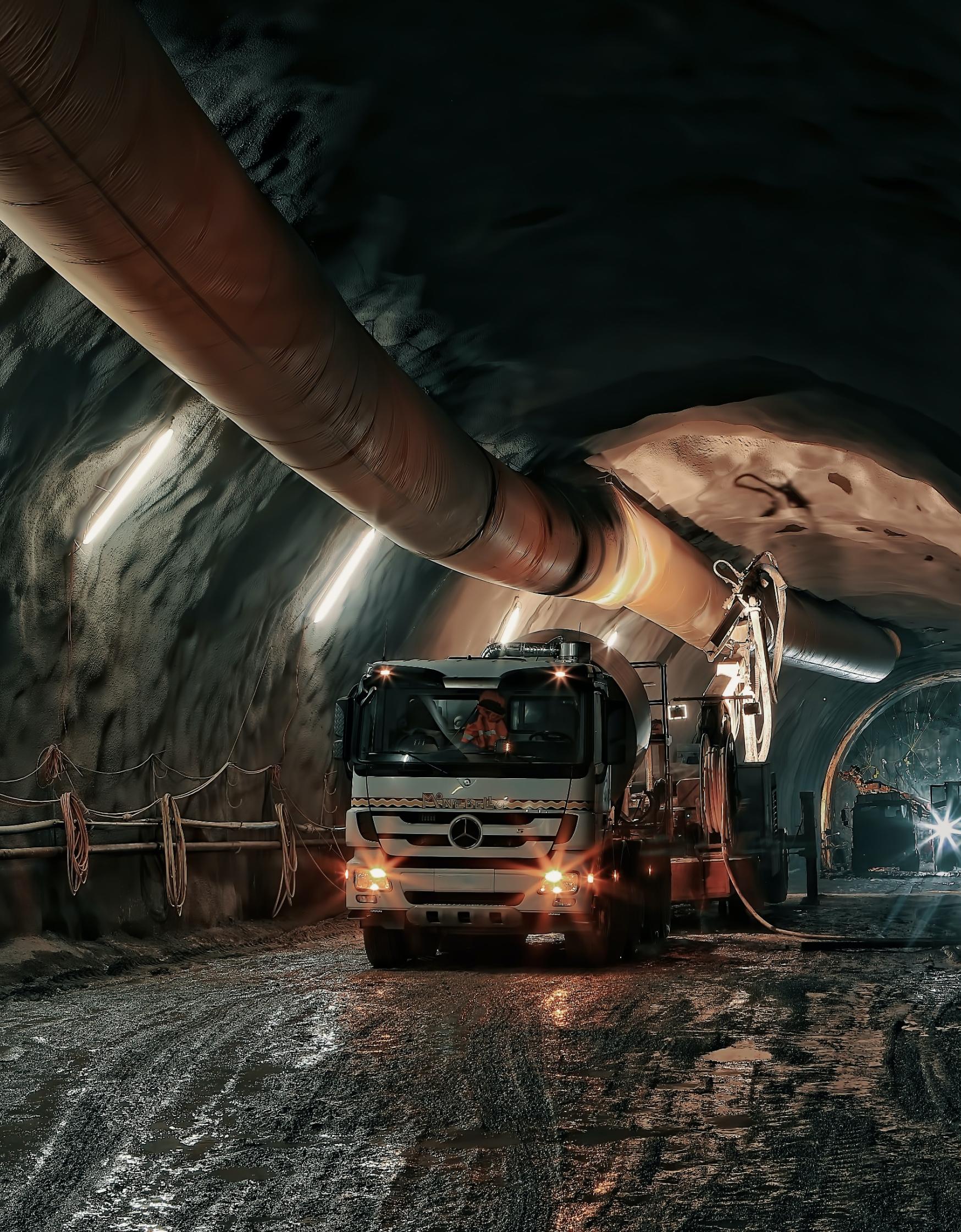 A truck parked in a mine with pipe running overhead.