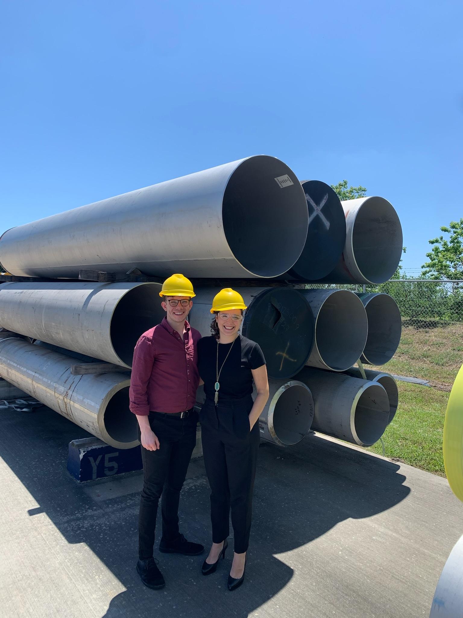 Two workers standing beside steel pipes and smiling.